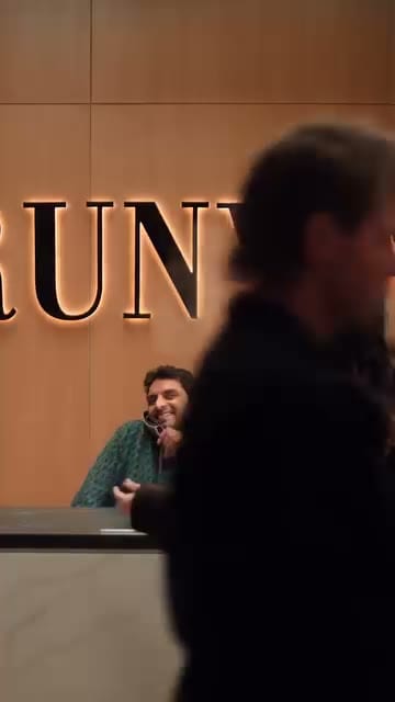 Get Noticed, RUNWAY-magazine reception desk, cinematic context-set; the viewer is reading a fashion-office world, not an ad.