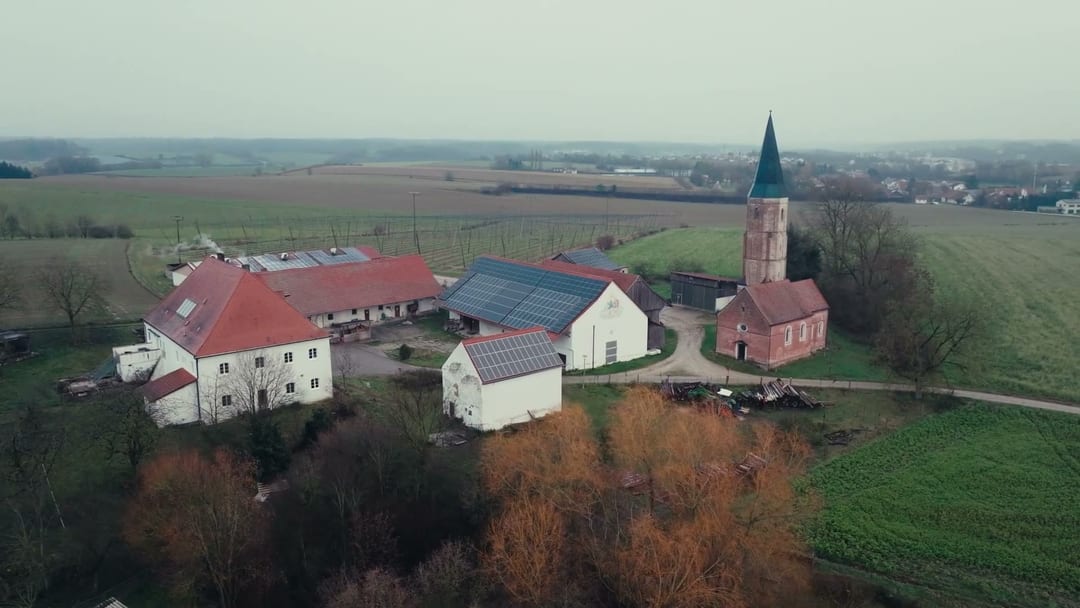 Brand Impact, Drone shot of a solar-paneled farmstead with a church spire, the 'electric / sustainable' story is being built, brand implicit.
